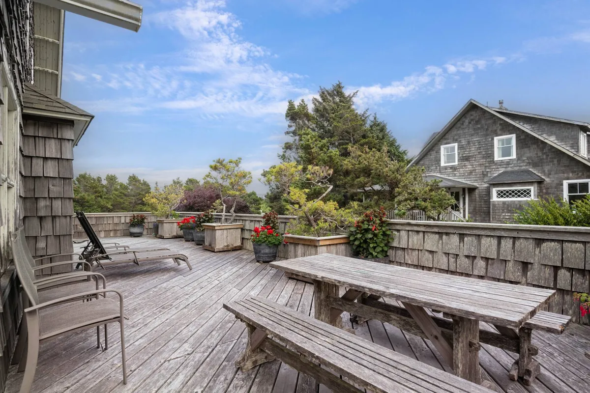 A tranquil and inviting wooden deck surrounded by flower pots and lush greenery. The view includes seating perfect for enjoying morning coffee or relaxing with friends, while the orientation suggests an ideal vantage point for sunset watching and peaceful moments in nature.