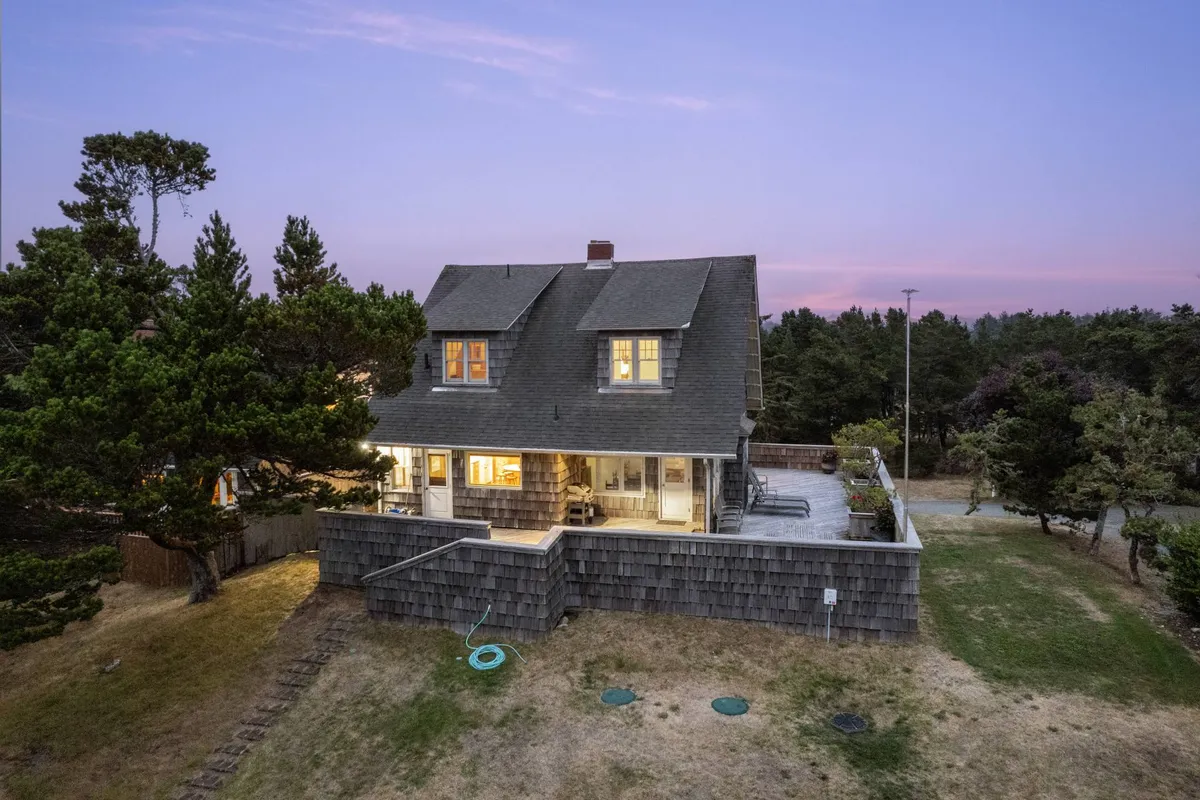 A warm, inviting view of Gin Ridge Cottage's exterior during sunset, featuring the charming front porch nestled among mature trees. The porch is adorned for relaxation, and the glowing light suggests cozy evenings inside.