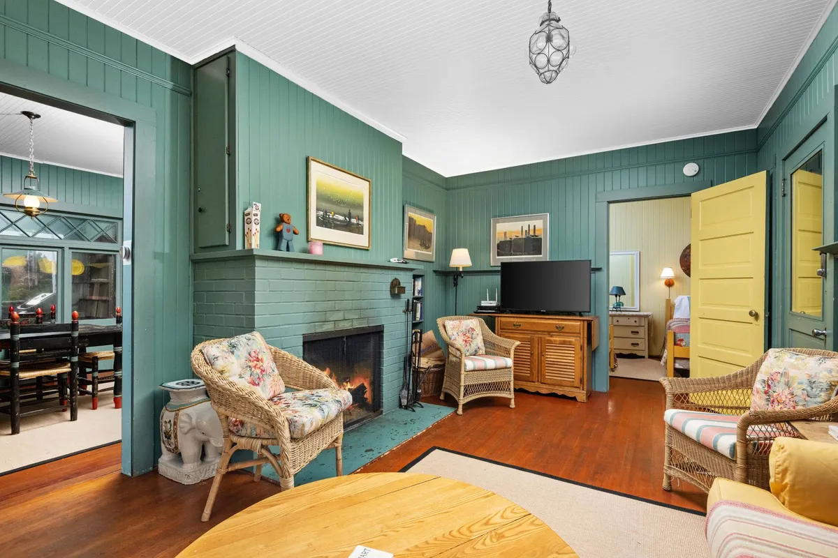 A cozy living room centered around a classic wood-burning fireplace, surrounded by ample, comfortable seating and adorned with decorative wall art. The warm tones and inviting arrangement make it easy to imagine evenings spent socializing, watching TV, or snuggling up by the fire.