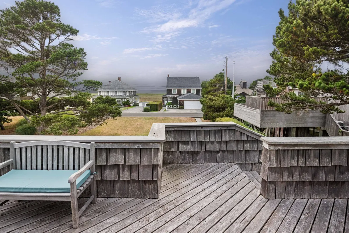A peaceful exterior scene featuring a wooden deck with a comfortable chair overlooking the surrounding natural landscape. The view suggests an ideal spot for relaxing, enjoying the scenery, or whale watching during the migration season. The setting is tranquil, inviting guests to spend quiet mornings outdoors.
