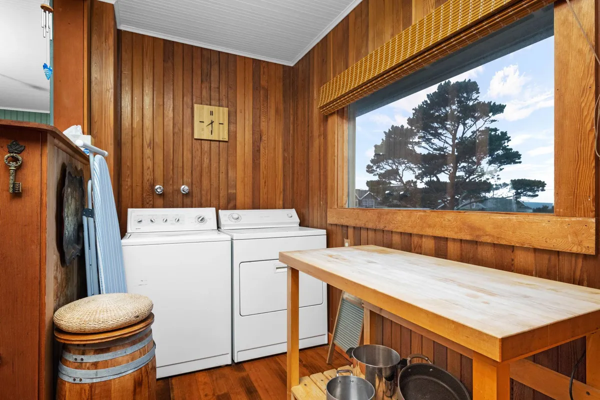 This image features a well-lit laundry area with a washing machine and dryer, a sturdy wooden table, and a large window that brings in natural light. The setup appears practical and inviting, demonstrating the convenience available for extended stays.