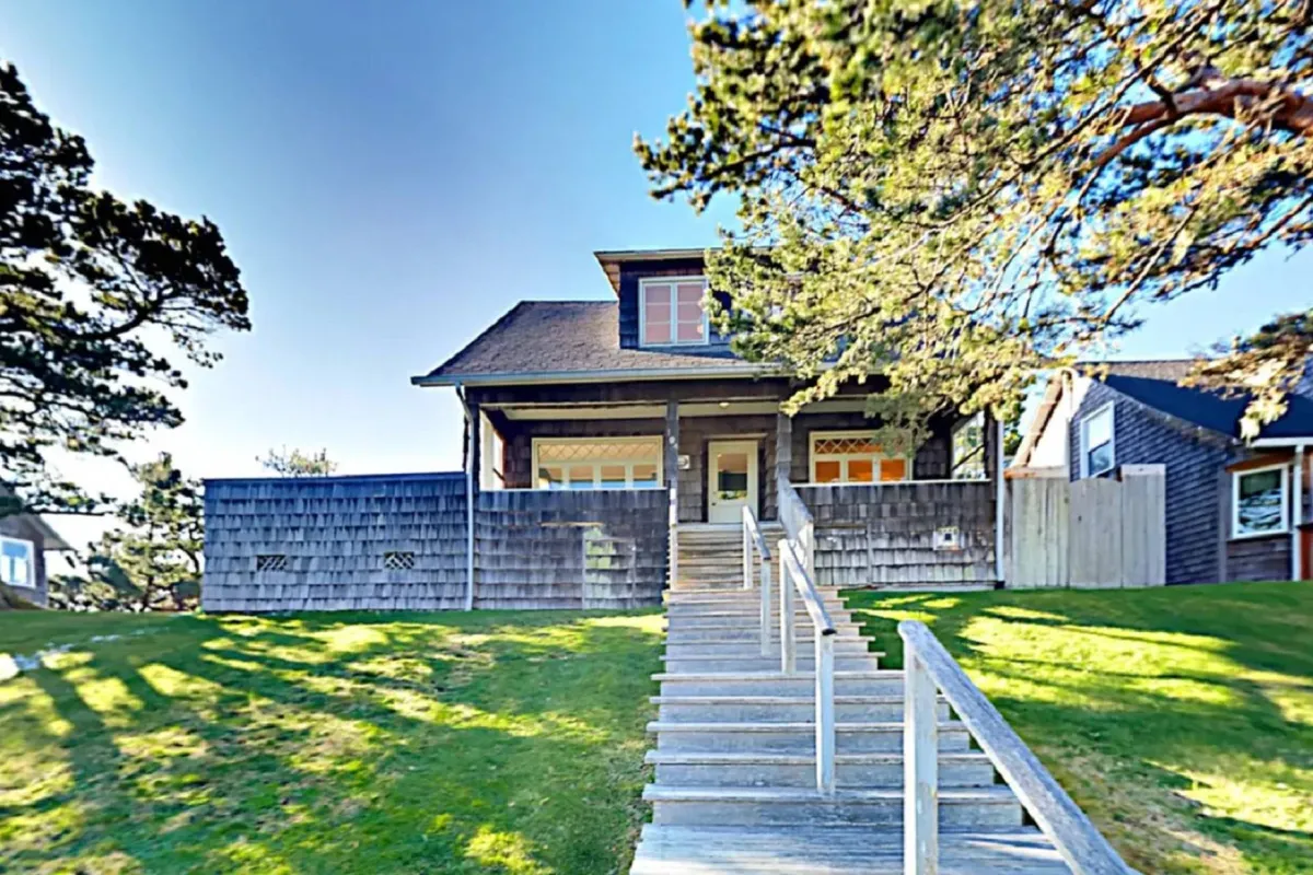 A closer look at the inviting front porch, complete with staircase and large windows under a leafy canopy, setting the scene for morning coffee or evening drinks outdoors.
