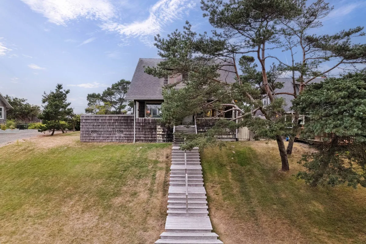 A view of the house's wooden pathway flanked by tree branches, leading up to the charming facade. The natural setting and architectural details evoke a sense of historic character, while the open pathway suggests opportunities for exploration and peaceful strolls.
