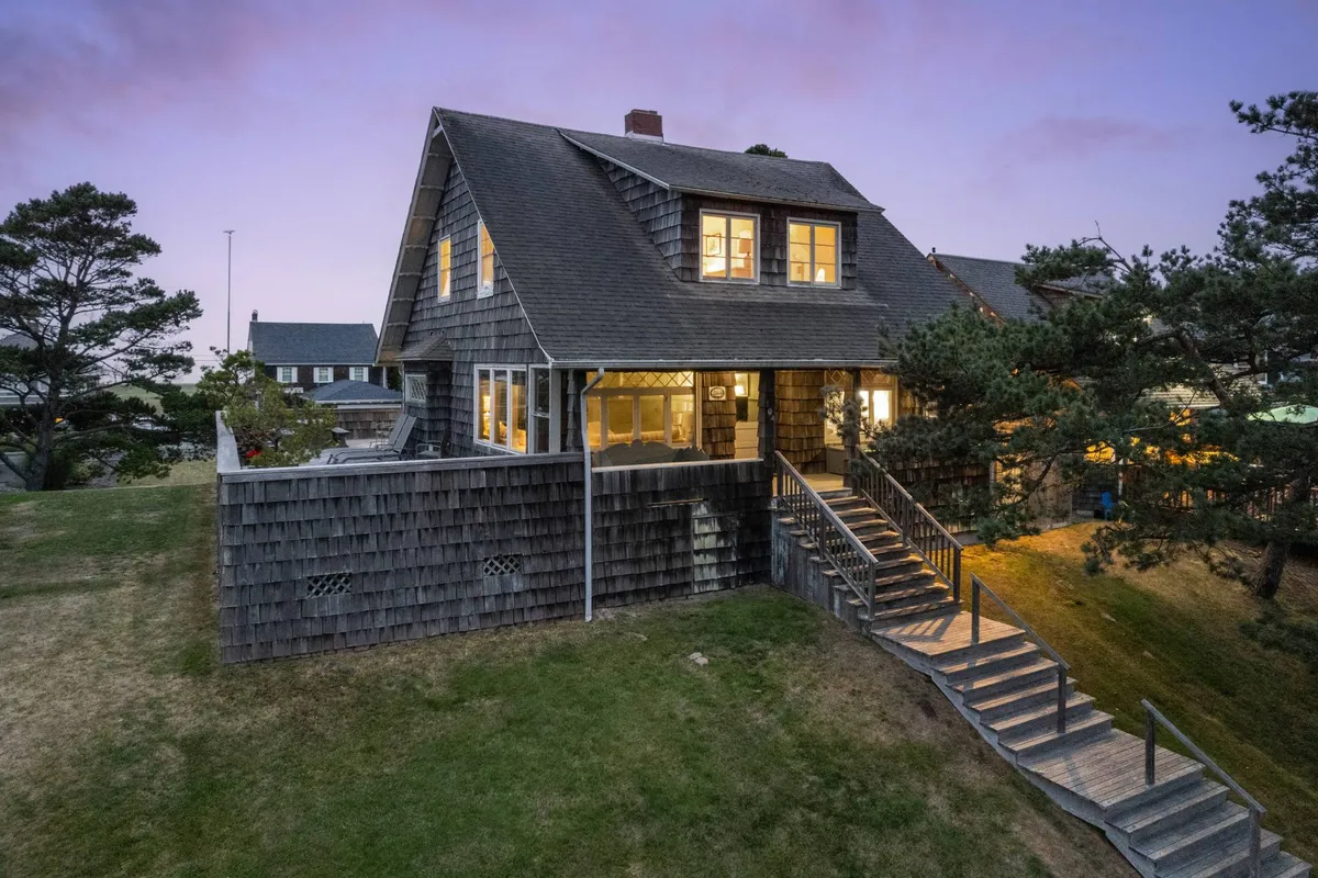 The inviting exterior of Gin Ridge Cottage, with warm, illuminated windows and a welcoming staircase leading up to the entrance. The outdoor space hints at gatherings and the easy transition between home and nature.